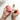 A person applies clear nail polish over bright pink nail polish on their fingernails, with a bottle of nail polish nearby on a white surface.
