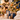 A festive Christmas tree decorated with gold and navy ornaments, ribbons, and warm string lights, with wrapped gift boxes placed underneath in a cozy, softly blurred holiday living room.