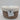 A small, round natural woven wicker storage basket from Bullseye’s Playground™ featuring a fitted white lid and a front label that reads “Natural Woven Wicker Storage Basket – Small w/ White Lid.” The background is plain white.
