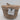 A small, round Natural Woven Wicker Storage Basket with a wicker lid from Bullseye’s Playground™ is shown against a plain white background. The basket features a white label on the front that reads “Natural Basket with Lid.”.