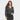 A woman with long brown hair wears a Universal Thread™ Women's Long Sleeve Smocked Blouse in Black Floral and a dark denim skirt, standing against a white background with one hand in her pocket and a neutral expression.