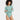 A woman with curly hair wears the Auden Women's Luxury Collection 4-Way Stretch Long Sleeve Bodysuit in Tidal Flow, standing with arms crossed and smiling to the side against a plain white background.