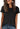 A person wearing a black Women’s Wrinkle-Free Short Sleeve Crew Neck T-Shirt tucked into blue jeans.