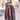 A person wears a Women’s Oversized Plaid Winter Blanket Scarf Pink, Black & Red in an oversized, fringed red, pink, and white plaid pattern over a textured corduroy quarter-zip pullover.