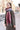 A person wears a Women’s Oversized Plaid Winter Blanket Scarf Pink, Black & Red in an oversized, fringed red, pink, and white plaid pattern over a textured corduroy quarter-zip pullover.